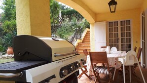 An outdoor patio with a barbecue grill, a dining table with chairs, and a staircase leading to an upper level.