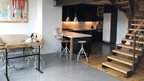 Une cuisine moderne dotée d’un îlot central, d’un coin repas avec une table et des chaises en bois, et d’un escalier menant à un niveau supérieur.