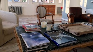 Un salon chaleureux avec une table basse en bois sur laquelle sont posés des livres et des bougies, un fauteuil en cuir et une vue sur les montagnes par de grandes fenêtres.