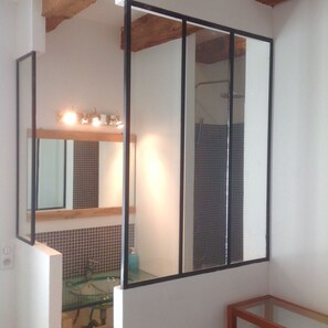 A bathroom with a large mirror, a glass shower enclosure, and a tiled backsplash.