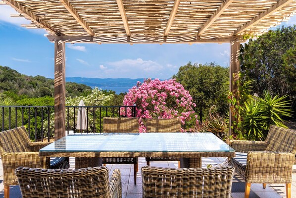 An outdoor patio with wicker furniture, a glass table, and a view of the landscape.