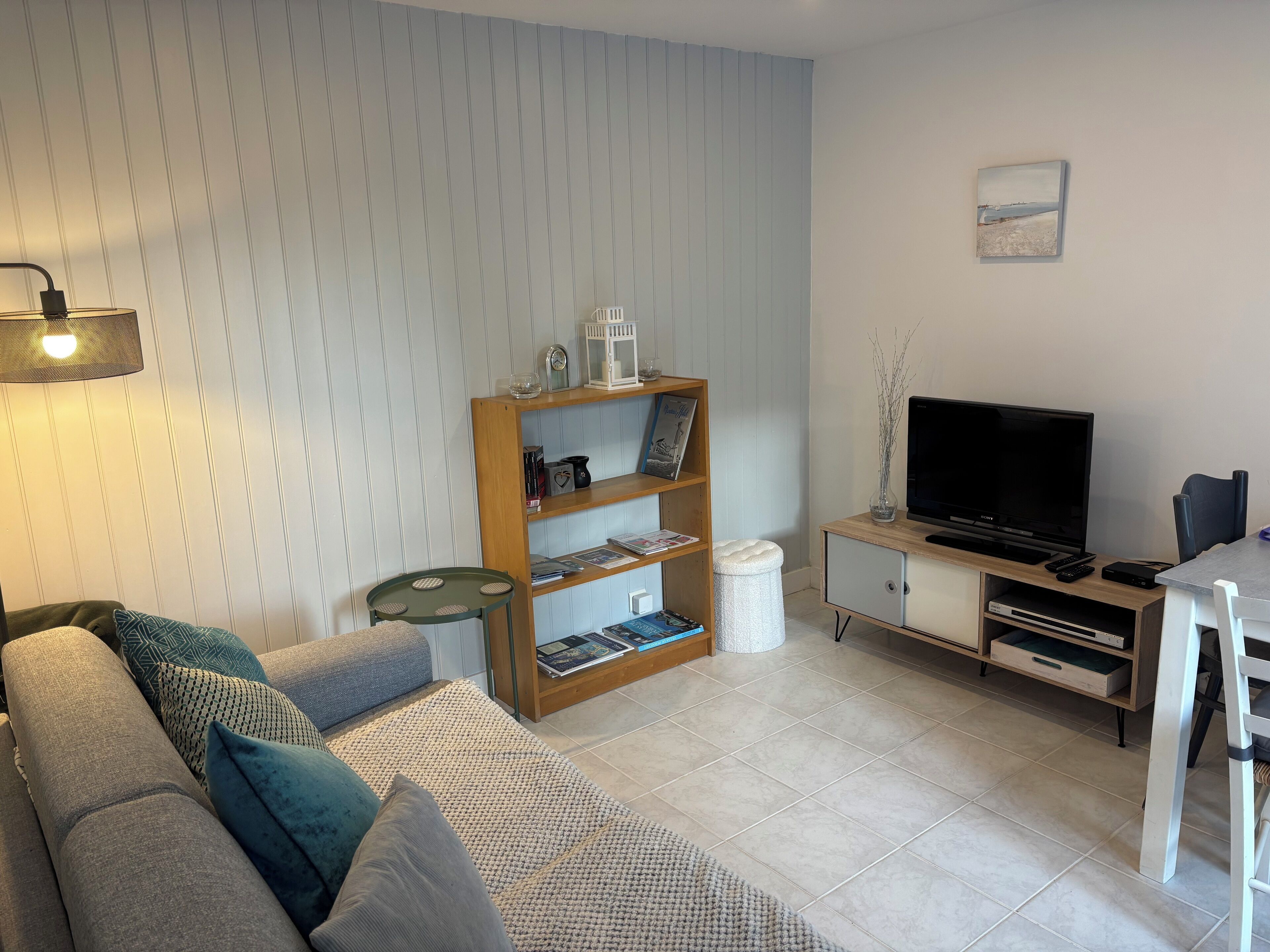 Una sala de estar con un sofá, una mesita, una estantería, un televisor y un mueble de almacenamiento.