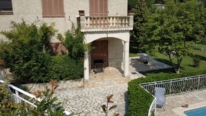 Eine Villa mit einer Steinterrasse, einem Pool und einem Garten.