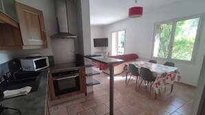 Eine kompakte Küche mit Mikrowelle, Herd und Abluftvorrichtung. Es gibt einen Essbereich mit Tisch und Stühlen sowie ein Fenster mit Blick auf Grünflächen.