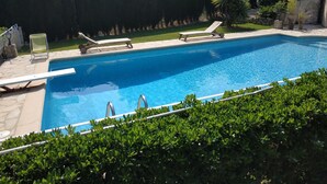 Ein rechteckiger Pool mit glasklarer, blauer Wasseroberfläche, umgeben von einer Steindeck. Auf dem Deck befinden sich zwei Liegestühle und ein kleiner Tisch.