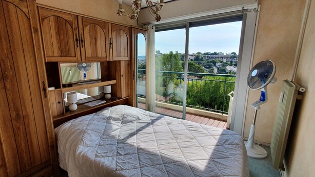 Un dormitorio con una cama grande, armarios de madera, un balcón con vistas y un ventilador de pie.