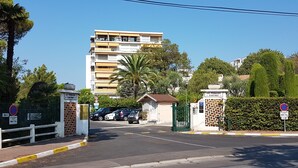Un conjunto residencial cerrado con un edificio de varios pisos, una caseta de vigilancia pequeña y automóviles estacionados.