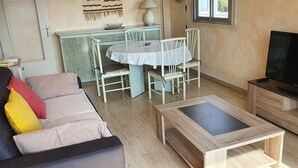 Una sala de estar con un sofá, una mesa de centro, un televisor, una mesa de comedor con sillas y una zona de cocina con una lámpara.