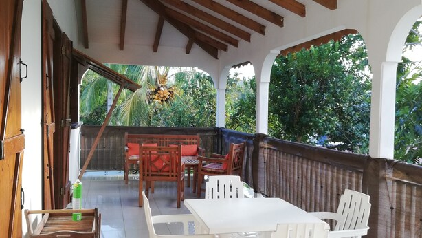 A covered outdoor dining area with wooden furniture and a tiled floor. - Maisoson 130m in Sainte-Rose for the holidays at the seaside, mountains. (Sainte-Rose)