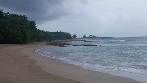 A beach with footprints leading to the water, a cloudy sky, and a distant shoreline with vegetation. - Maisoson 130m in Sainte-Rose for the holidays at the seaside, mountains. (Sainte-Rose)