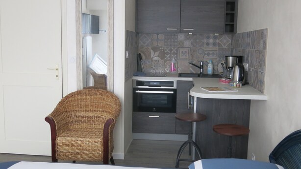 Cocina compacta con microondas, horno y cafetera. Hay dos taburetes y una silla de mimbre.