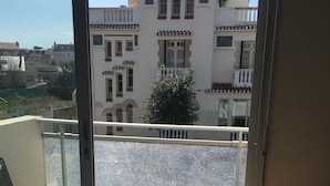 Un balcón con una silla de mimbre, una mesita y vistas a edificios.