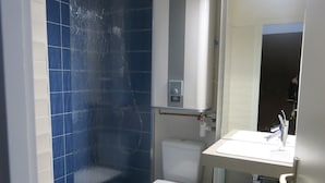 Un baño con inodoro blanco, lavabo con espejo y zona de ducha con azulejos azules.