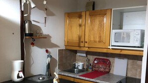 Cocina compacta con armarios de madera, microondas, cafetera y refrigerador pequeño.