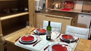 Una mesa de comedor dispuesta para cuatro personas, con platos rojos y blancos, copas de vino y una botella de vino.