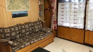 Un interior de madera con un sofá estampado, un mapa en la pared y una ventana con cortinas.