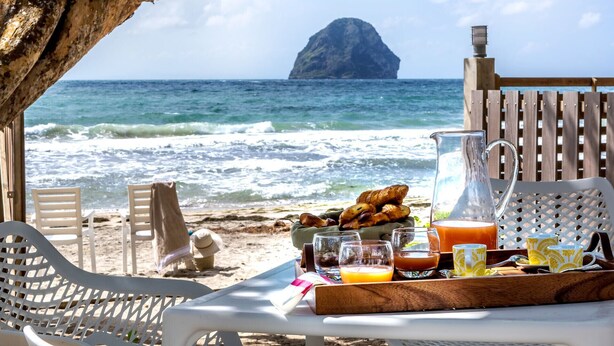 A beachside breakfast setup with a view of the ocean and a distant island. - La Régence (Le Diamant)
