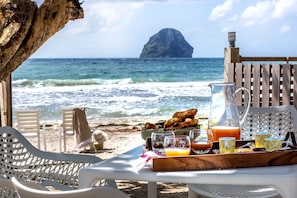 A beachside breakfast setup with a view of the ocean and a distant island. - La Régence (Le Diamant)