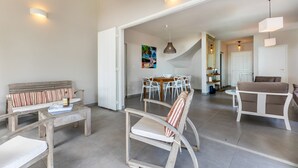 A spacious living area with a dining table, chairs, and a sofa. There is a staircase leading to another level. - La Régence (Le Diamant)