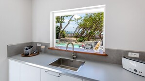 A modern kitchen with a built-in sink, a window overlooking a pool and greenery, and a Bosch appliance on the counter. - La Régence (Le Diamant)