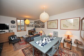 Een eetgedeelte met een tafel, stoelen, een hanglamp en een muur met ingelijste foto’s.