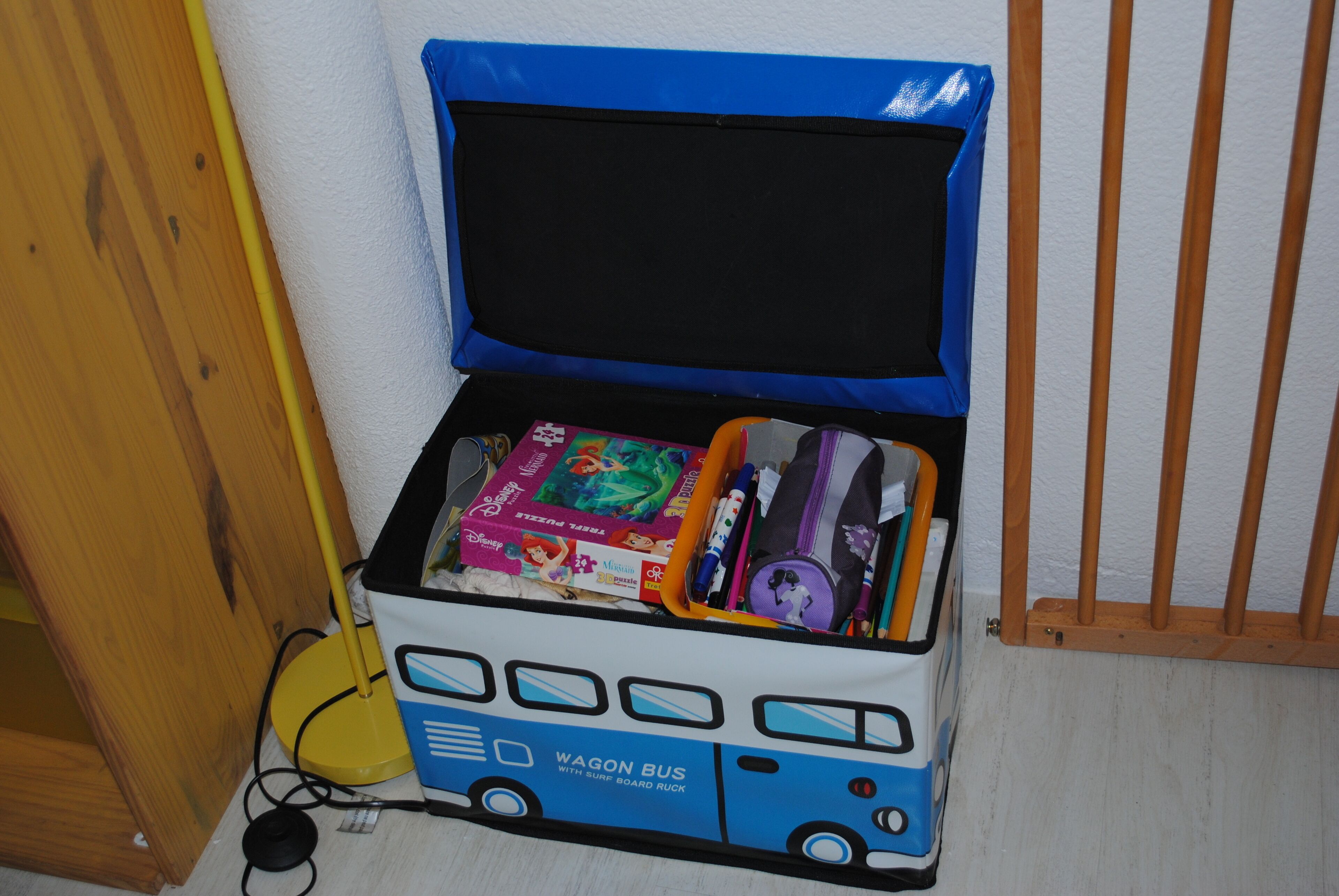 Caixa organizadora em forma de autocarro azul e branca, com tampa preta, contendo vários objetos como livros e um brinquedo.