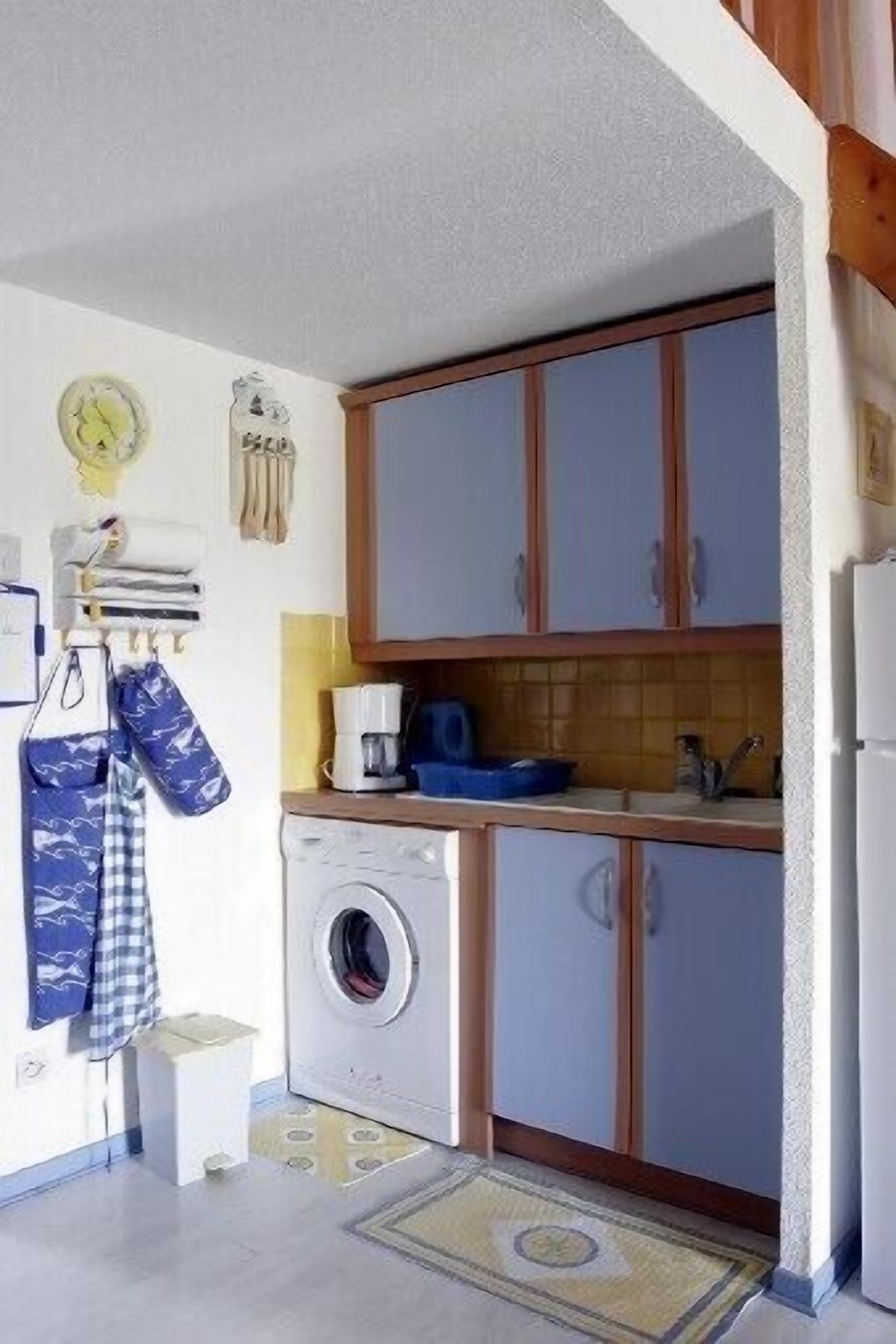A compact kitchen with wooden cabinets, a washing machine, and a coffee maker.