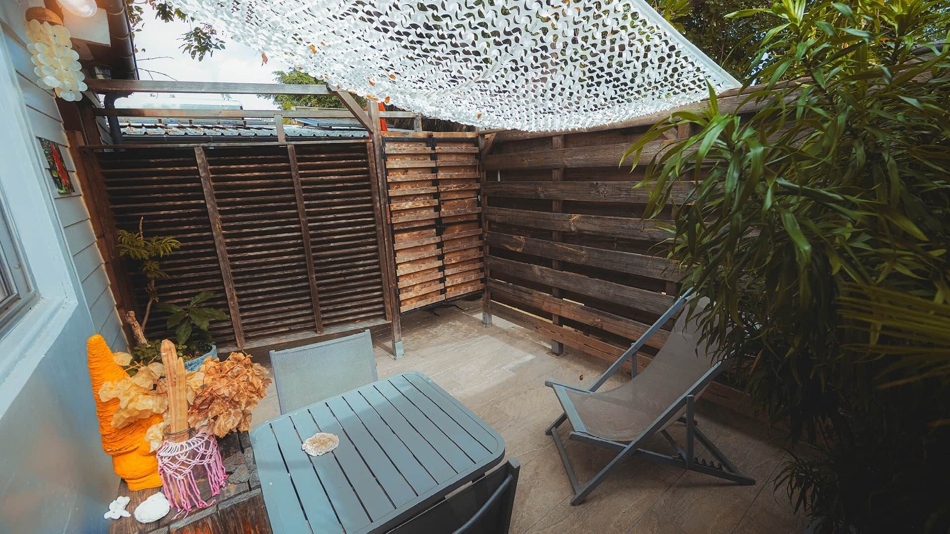 A small patio area with a wooden fence, a table, a chair, and a decorative umbrella.