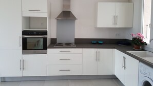 A modern kitchen with white cabinets, a stainless steel range hood, a built-in oven, and a washing machine. - 50 m2 apartment with terrace on the ground floor of a villa (Calvi)