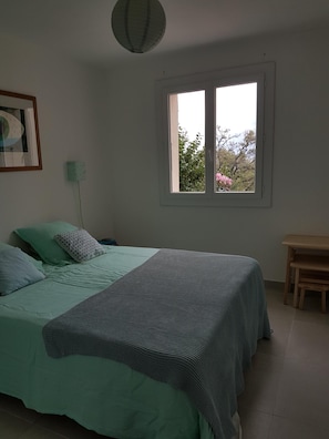 A bedroom with a bed, a window, a bedside table, and a lamp.