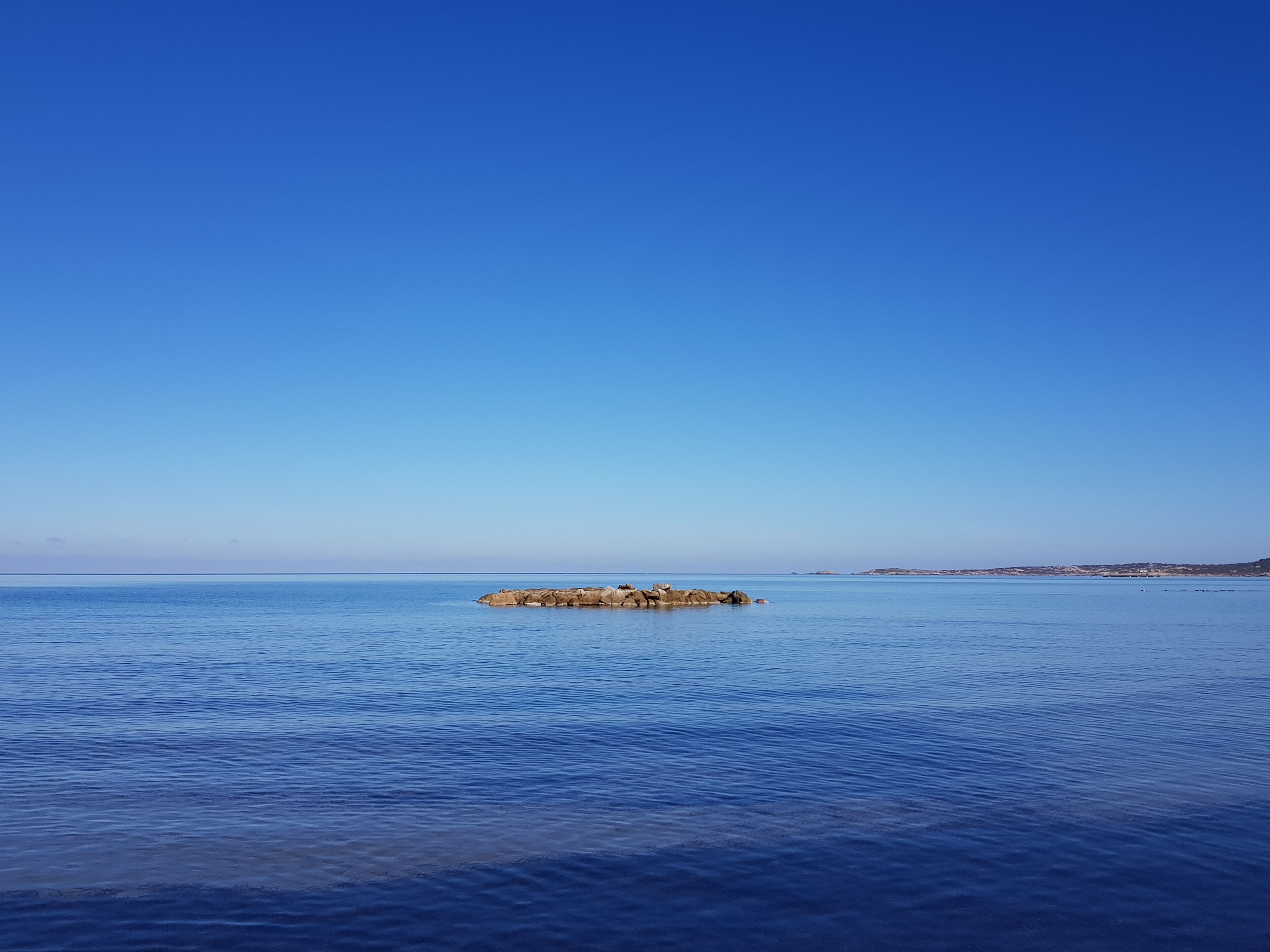 A calm sea with a rocky outcrop in the distance.