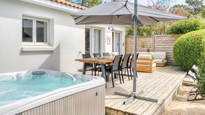 Un patio con jacuzzi, terraza de madera, mobiliario exterior y una pérgola con sombrilla.