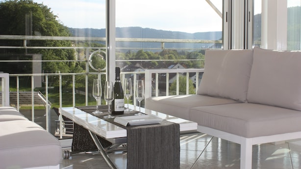 Un balcon avec un canapé blanc, une table en verre et une vue sur un paysage verdoyant.