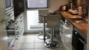 Une cuisine moderne avec une fenêtre, des appareils en acier inoxydable et un coin repas équipé de deux chaises.