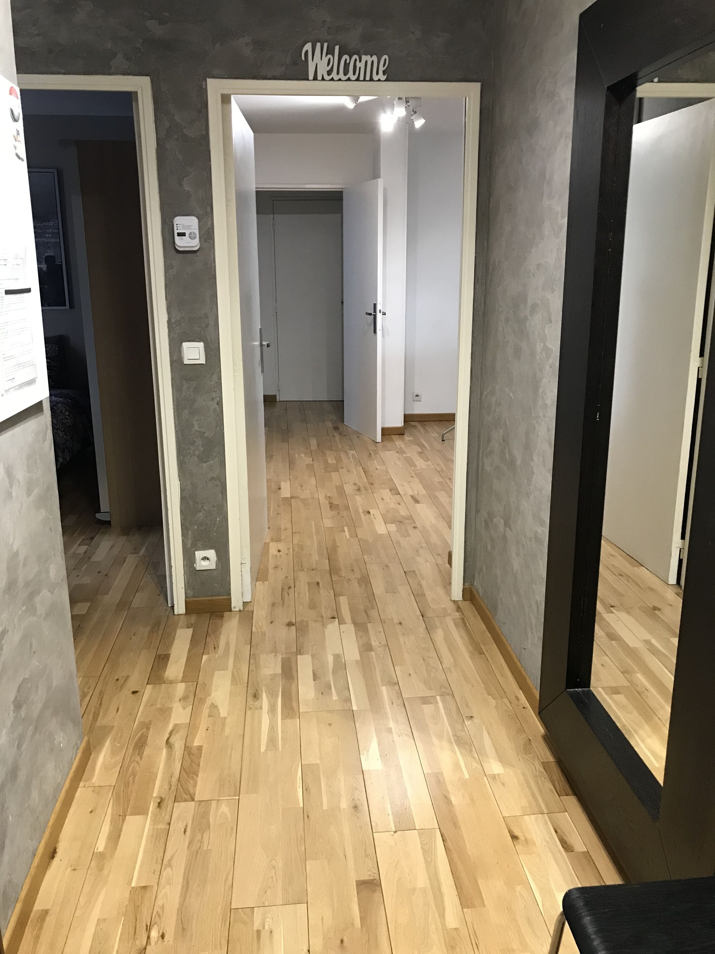 A hallway with a 'Welcome' sign, wooden flooring, and white walls.