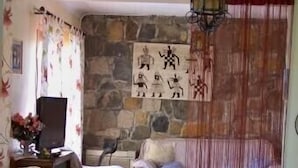 A cozy living room with wicker furniture, a stone wall, and a decorative hanging lamp. - Villa A LISCIA Marinca (Olmeto)