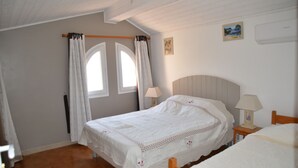 A bedroom with a bed, two bedside tables, a window with curtains, a wall-mounted air conditioner, and a small painting. - Villa A LISCIA Marinca (Olmeto)