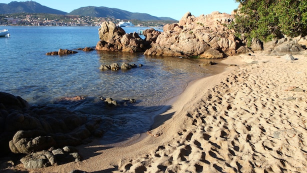 A beach with clear water, rocky formations, and a distant town. - Villa A LISCIA Marinca (Olmeto)