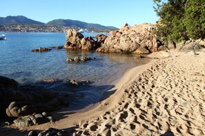 A beach with clear water, rocky formations, and a distant town.