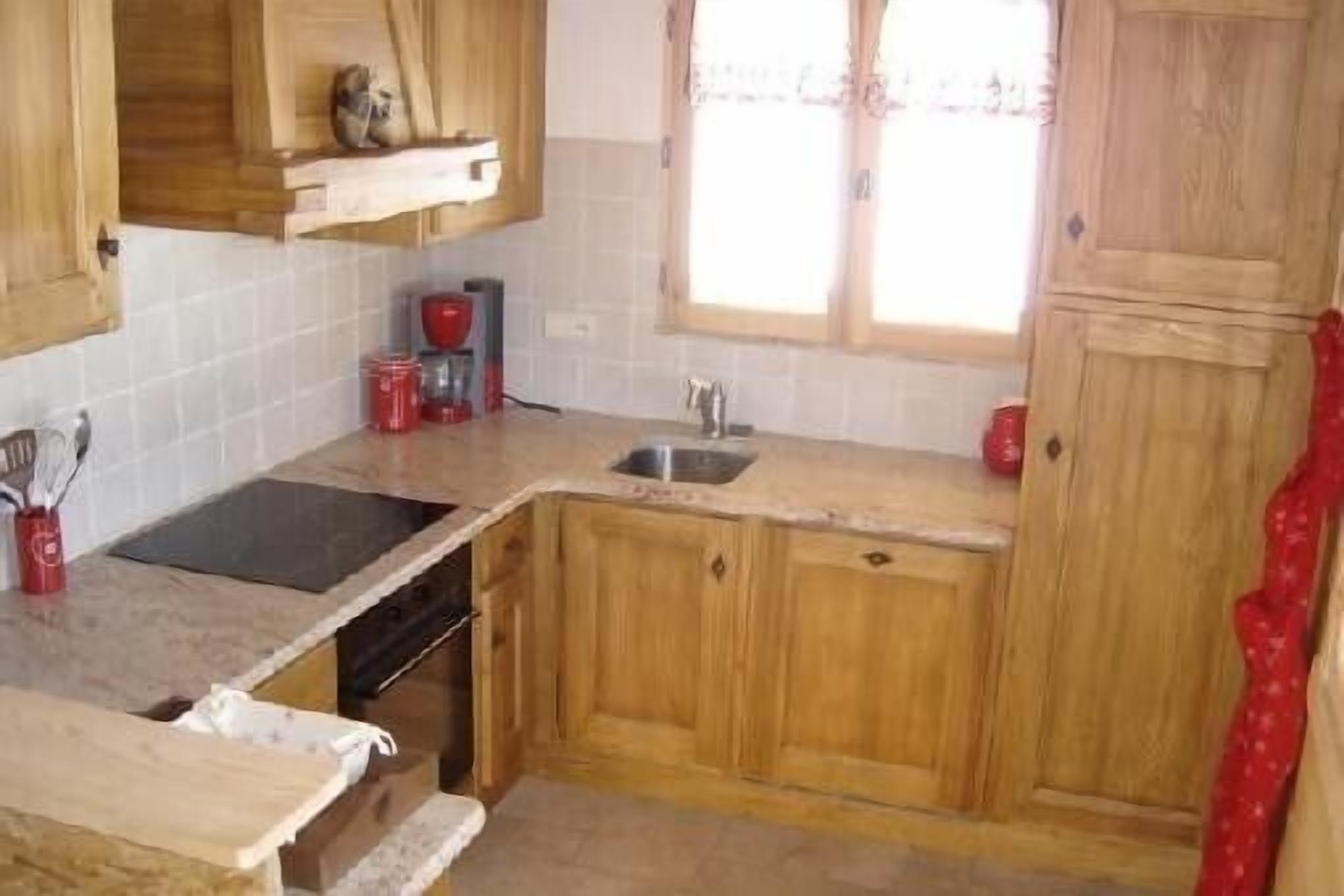 Une cuisine avec des meubles de rangement en bois, un plan de travail, un évier et une fenêtre avec des rideaux.