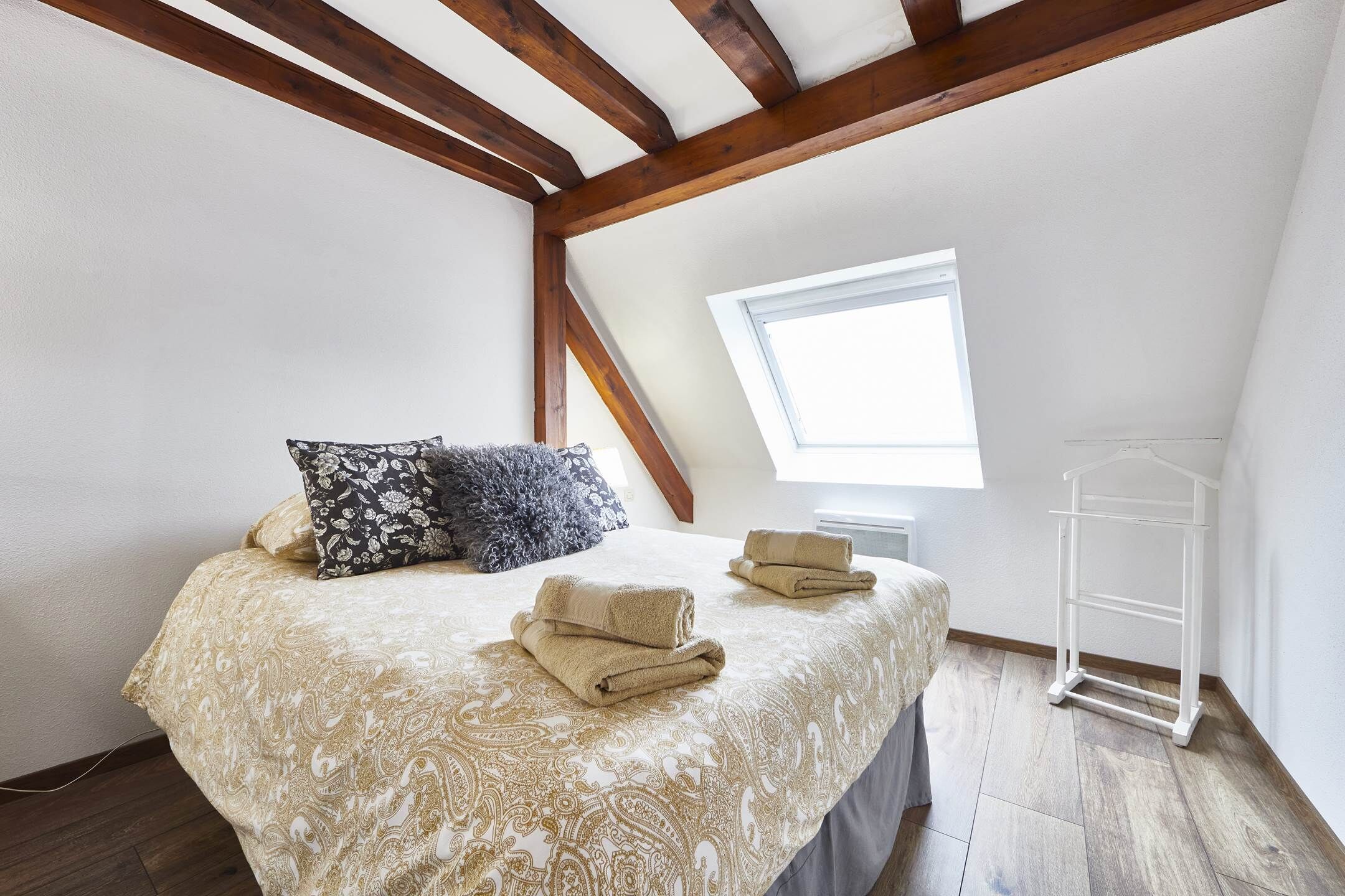 A bedroom with a bed, pillows, towels, a window, and a white rack.