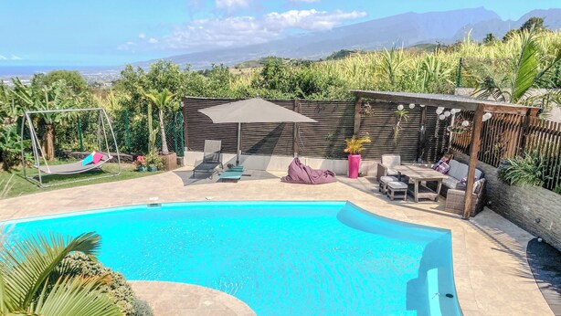 Une piscine à bordures courbes, entourée d’un patio aménagé avec des meubles d’extérieur et une pergola en bois.