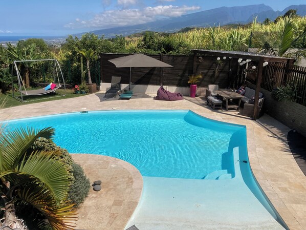 A swimming pool with a curved edge, surrounded by a patio area with seating and a pergola. - 15min from the beach, very well-equipped 4-person apartment***. (Saint-Pierre)