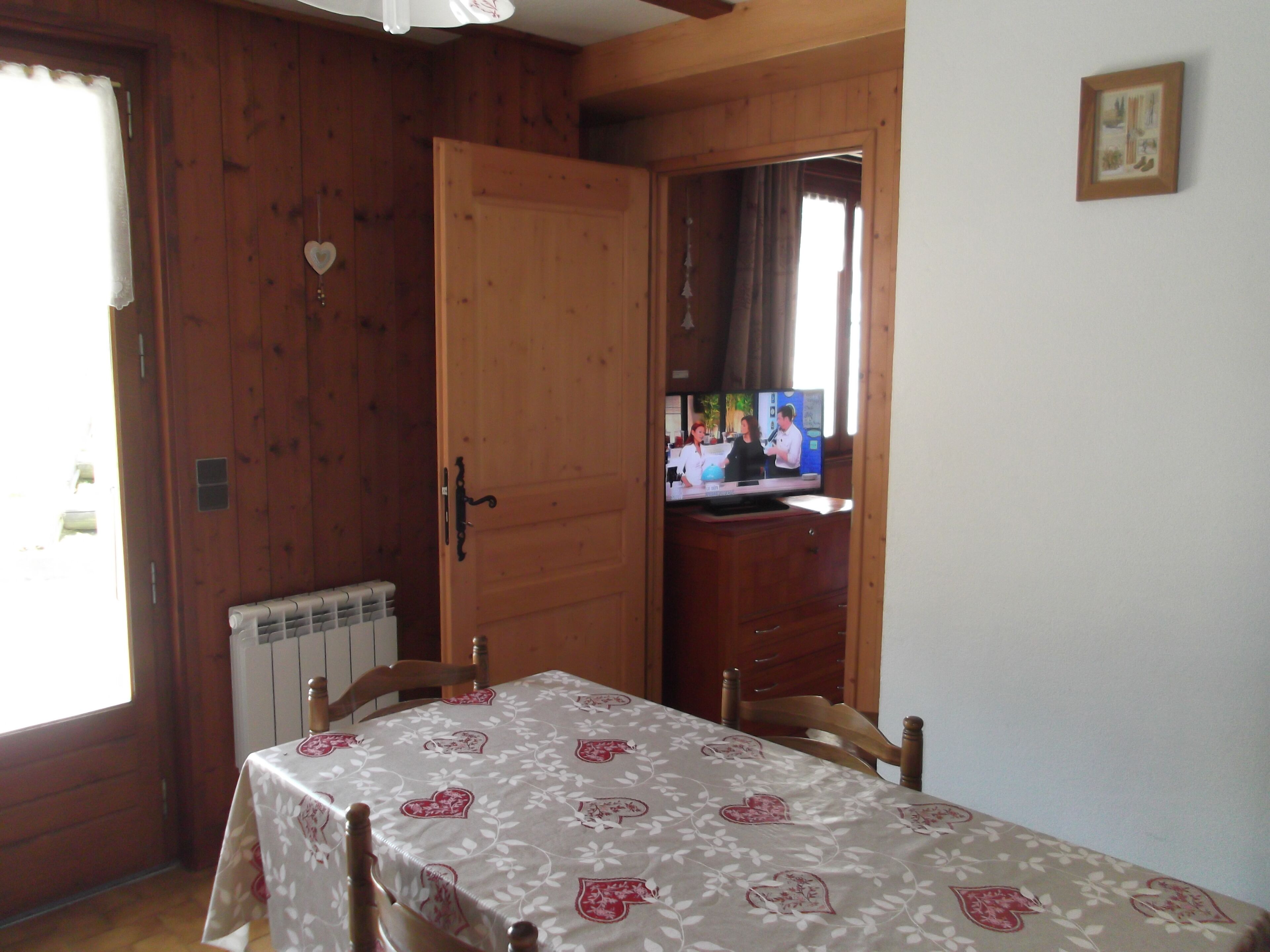 Um quarto de madeira com uma mesa coberta por um mantel decorada com flores, um radiador e uma televisão sobre um móvel de madeira.