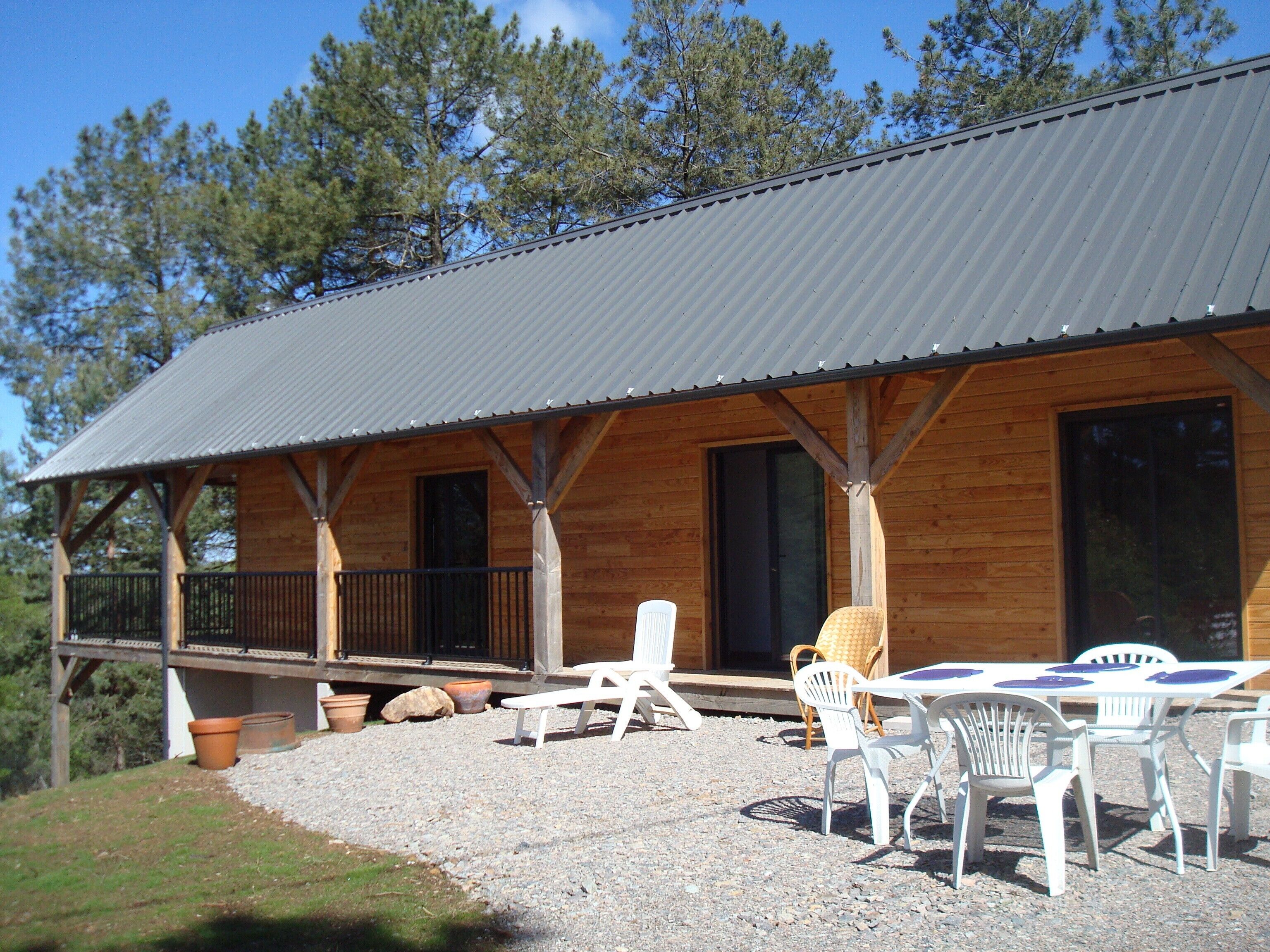 A wooden cabin with a covered patio, outdoor seating, and a gravel ground.