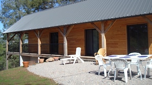 A wooden cabin with a covered patio, outdoor seating, and a gravel ground.