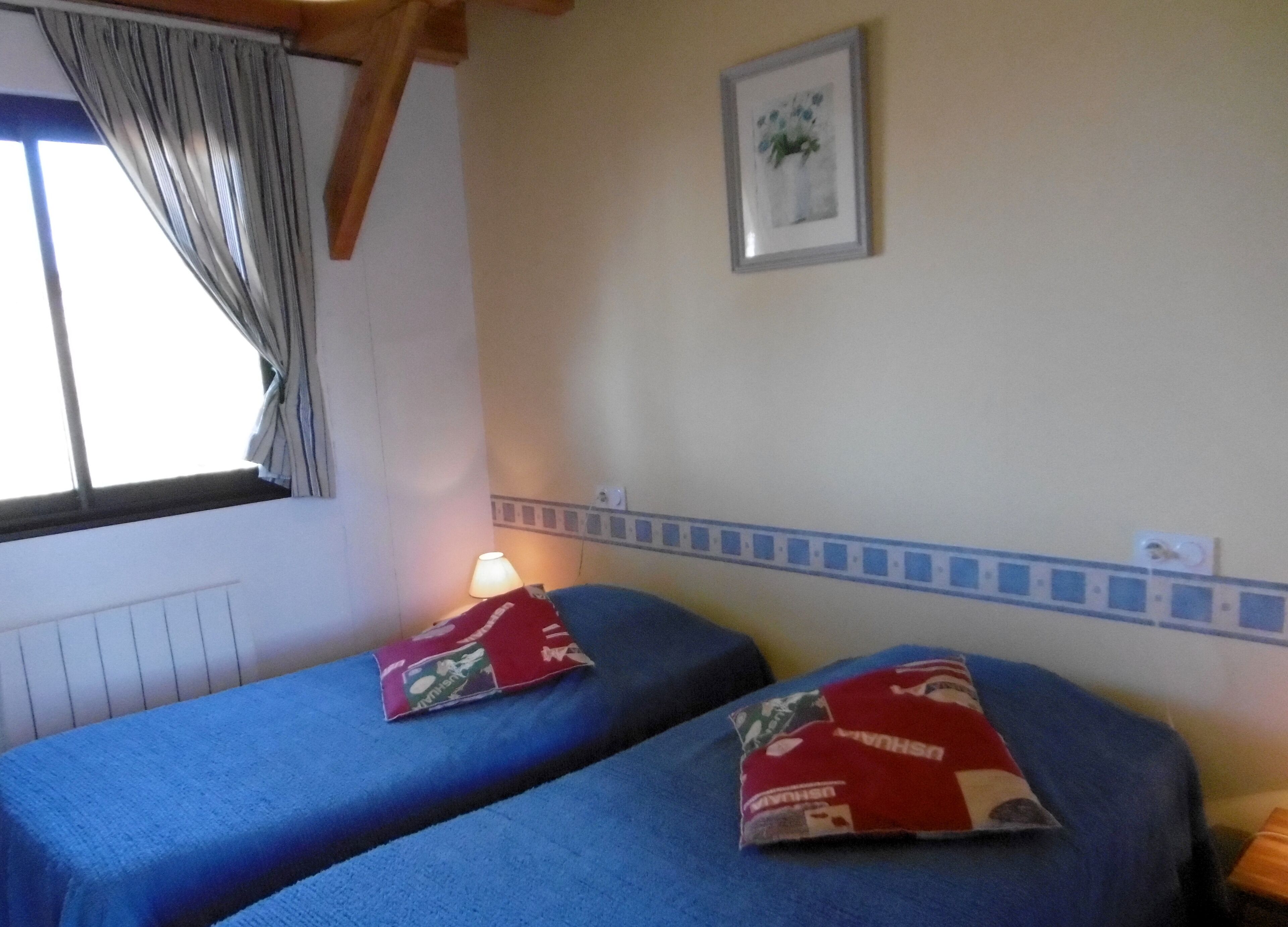 Una habitación con dos camas, una ventana con cortinas, una lámpara y un cuadro en la pared.