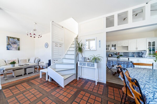 A spacious living area with a staircase leading to a kitchen, featuring white cabinetry and a tiled floor.