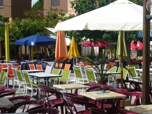 Outdoor seating with tables and chairs, umbrellas, and a small palm tree.