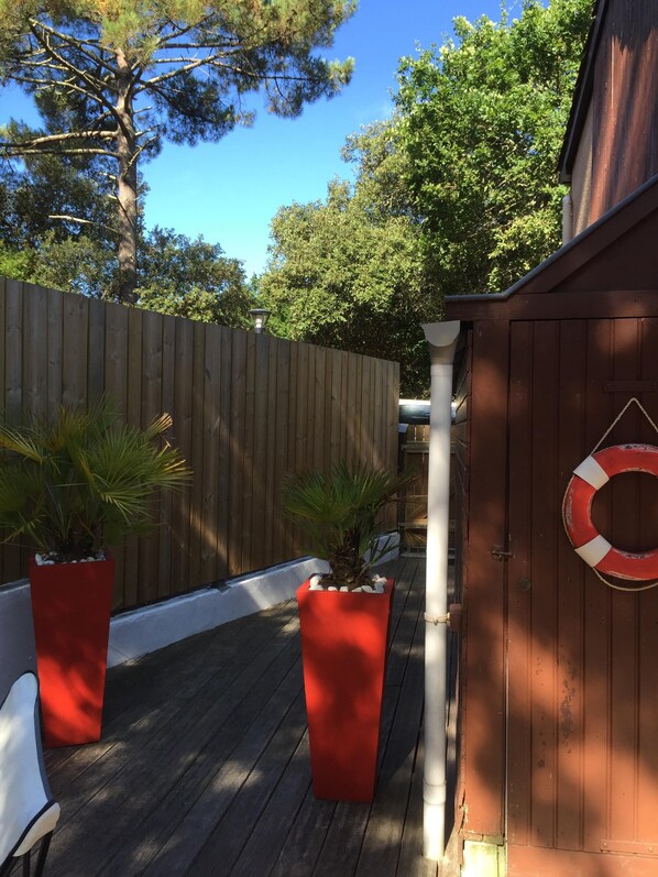 Une terrasse en bois agrémentée de deux jardinières rouges, d’une balustrade blanche et d’une clôture en bois.